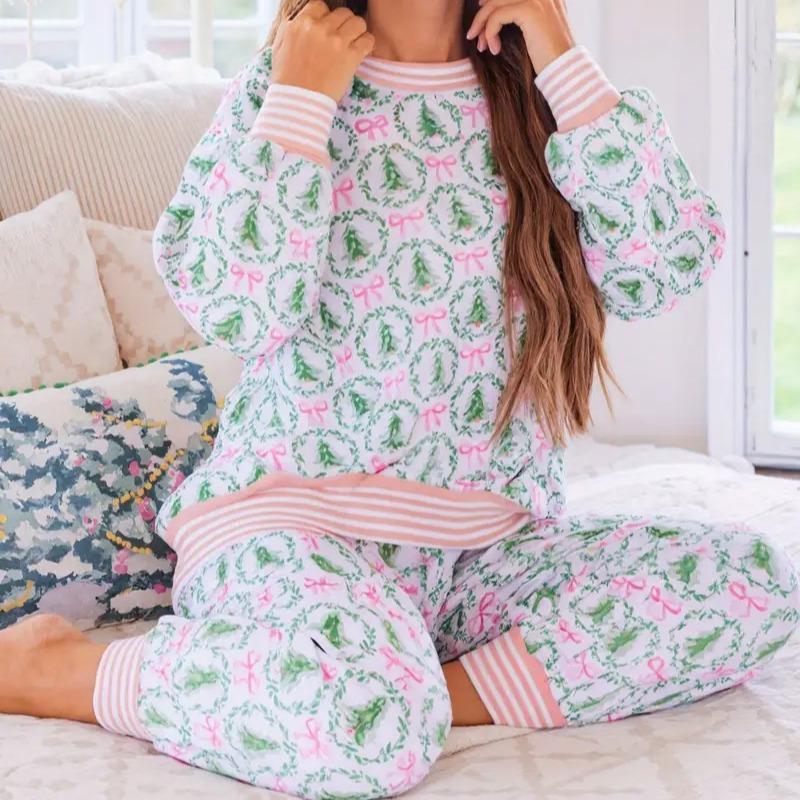 Person wearing a matching pajama set with green wreath and pink bow pattern on a couch.